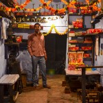 A man proudly poses in his shop, lavishly decorated for the festival of Diwali.